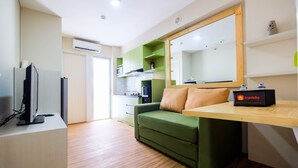 A modern hotel room with a green sofa, a wooden desk, a flat-screen TV, and a large mirror. - Connect to Pool 2BR Apartment at Bassura City (Jakarta)