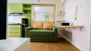A compact kitchen with green cabinets, a built-in stove, and a mirror above a green sofa with two cushions. - Connect to Pool 2BR Apartment at Bassura City (Jakarta)