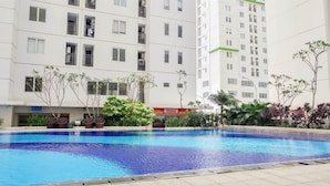 A swimming pool surrounded by a multi-story residential building with balconies and a visible storefront. - Connect to Pool 2BR Apartment at Bassura City (Jakarta)