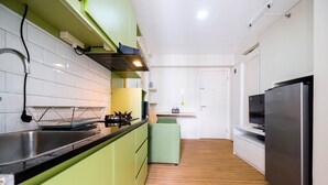 A modern kitchen with green cabinets, a stainless steel refrigerator, and a wooden floor. - Connect to Pool 2BR Apartment at Bassura City (Jakarta)
