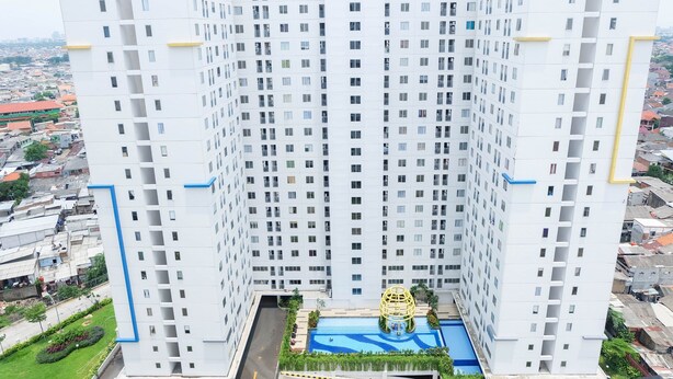 A high-rise building with a swimming pool at the base, surrounded by greenery. - Connect to Pool 2BR Apartment at Bassura City (Jakarta)
