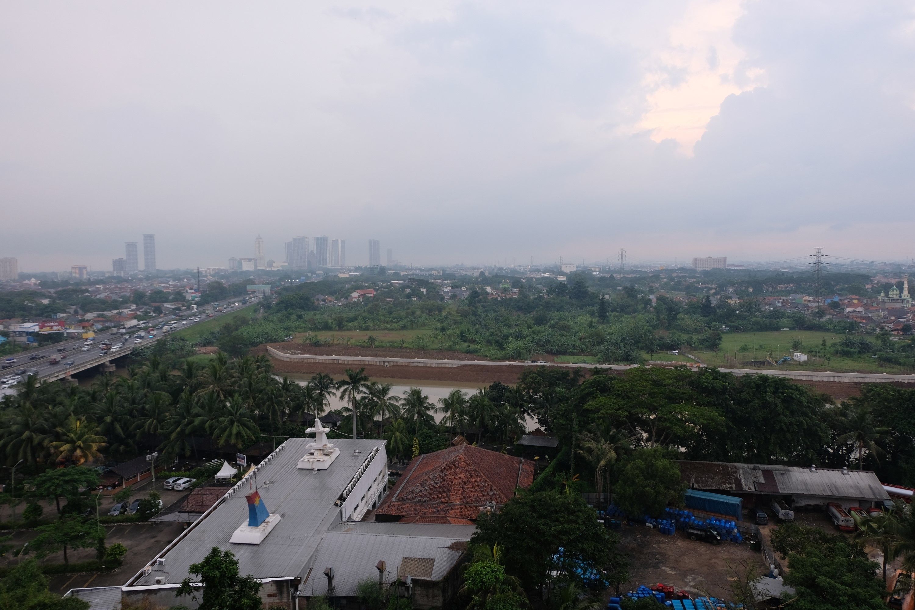 Vista panorámica de una ciudad con una mezcla de edificios residenciales y comerciales, una estructura blanca destacada con un campanario azul, y un río al frente.