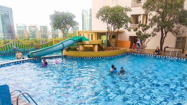 A swimming pool with a slide, surrounded by buildings and trees. - Minimalist Studio Room Great Western Apartment (Tangerang)