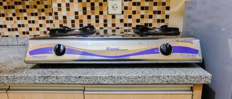 A kitchen with a Rinnai gas stove on a granite countertop, a tiled backsplash, and wooden cabinets.