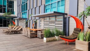 Ein moderner Außenbereich mit Korbmöbeln und einer Hängesessel, umgeben von Blumentöpfen und einem Gebäude mit großen Fenstern.