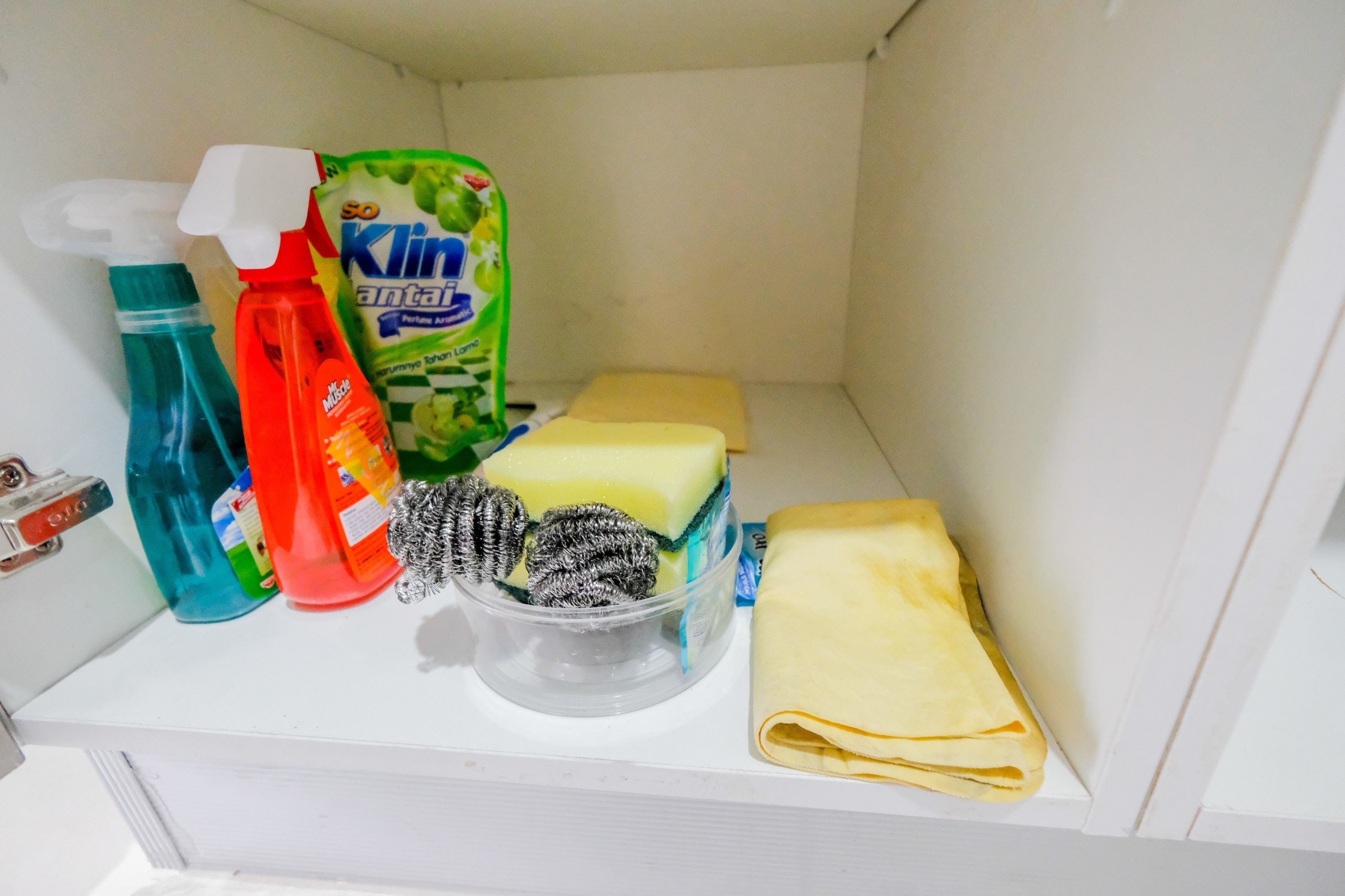 Un espace de rangement contenant des produits de nettoyage, un récipient rempli d’éponges et une serviette pliée.