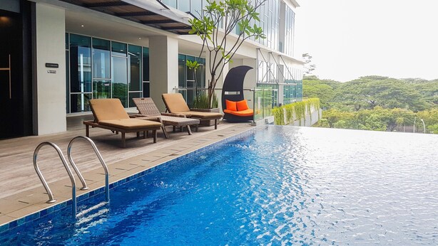 Ein modernes Hotel mit einem Dachpool im Infinity-Stil, Liegestühlen und Blick auf üppiges Grün.