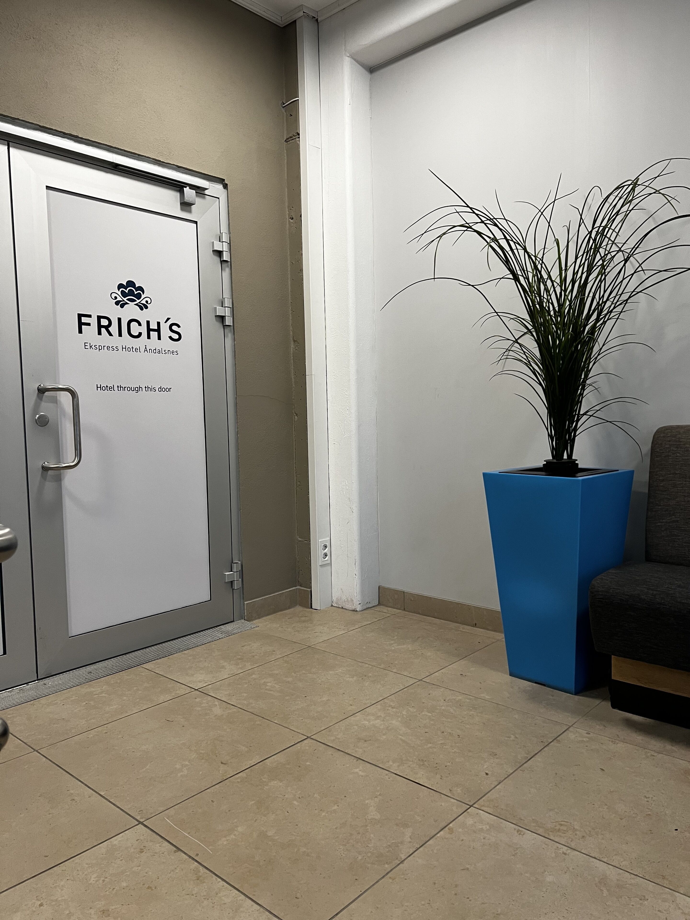 A hotel reception area with a closed door labeled "FRICH'S Ekspress Hotel Åndalsnes" and a potted plant beside a seating area.
