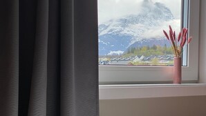Ett sovrum med en säng, ett fönster med utsikt över bergen och en vas med blommor på fönsterbrädan.