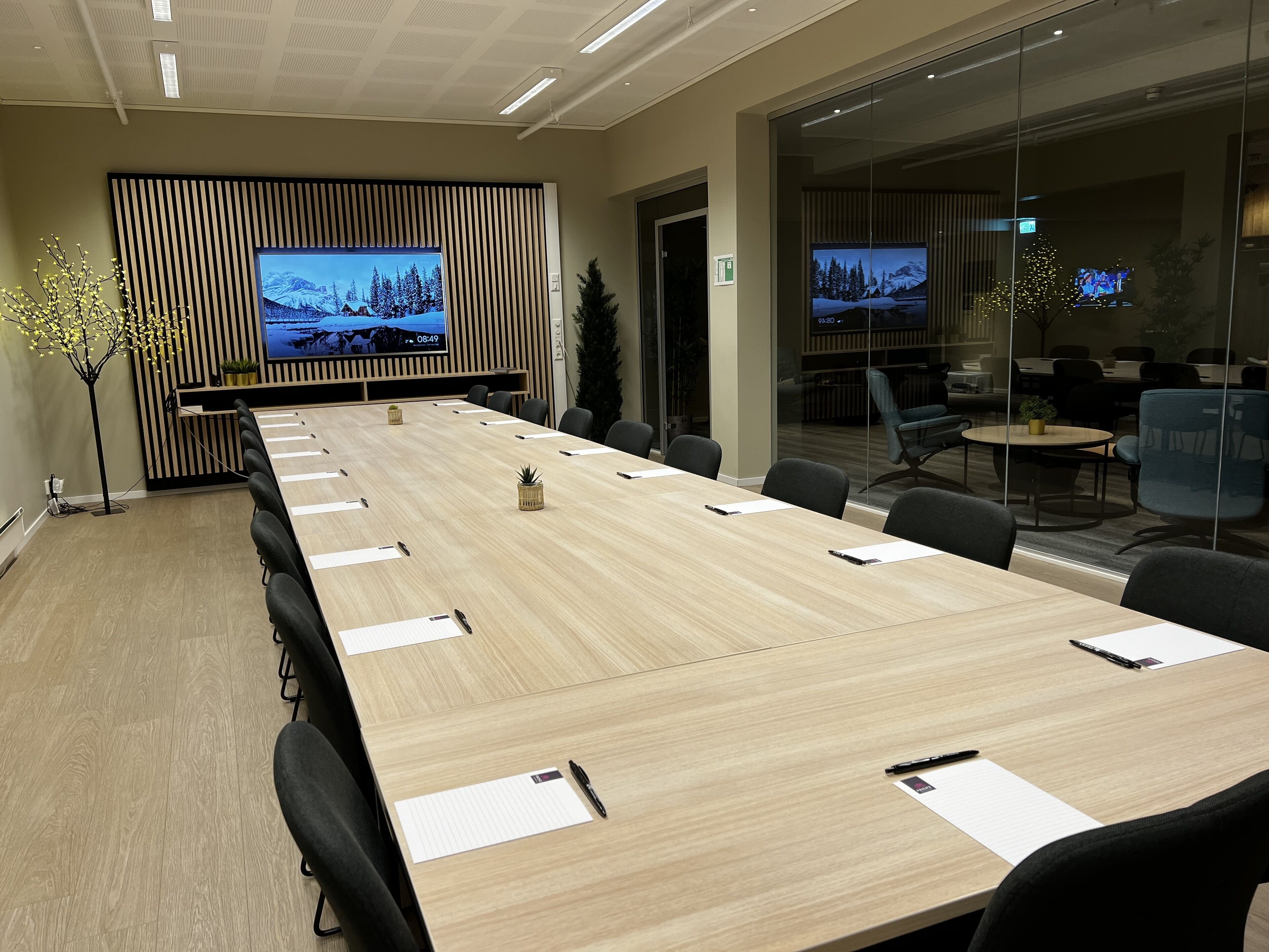 Un salón de conferencias con una larga mesa, sillas y una pantalla grande que muestra un paisaje nevado.
