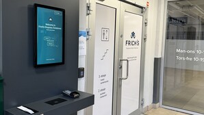En hotellreception med en digital skärm som visar ett välkomstmeddelande, en plats för att lämna in nycklar och dörrar som är märkta med vilken typ av rum de leder till.