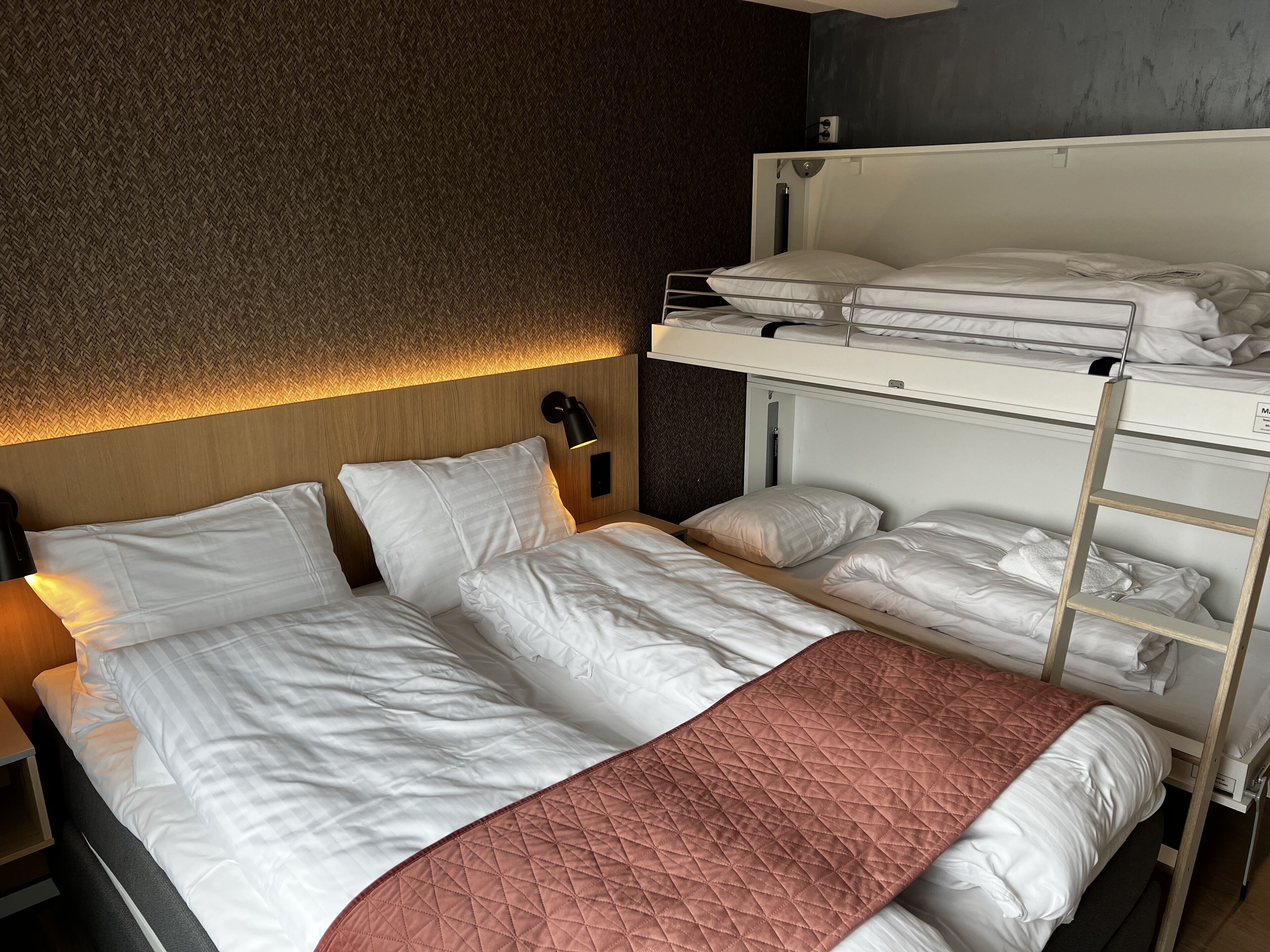 Een hotelkamer met een stapelbed, een enkel bed en een gewatteerde spreidek.