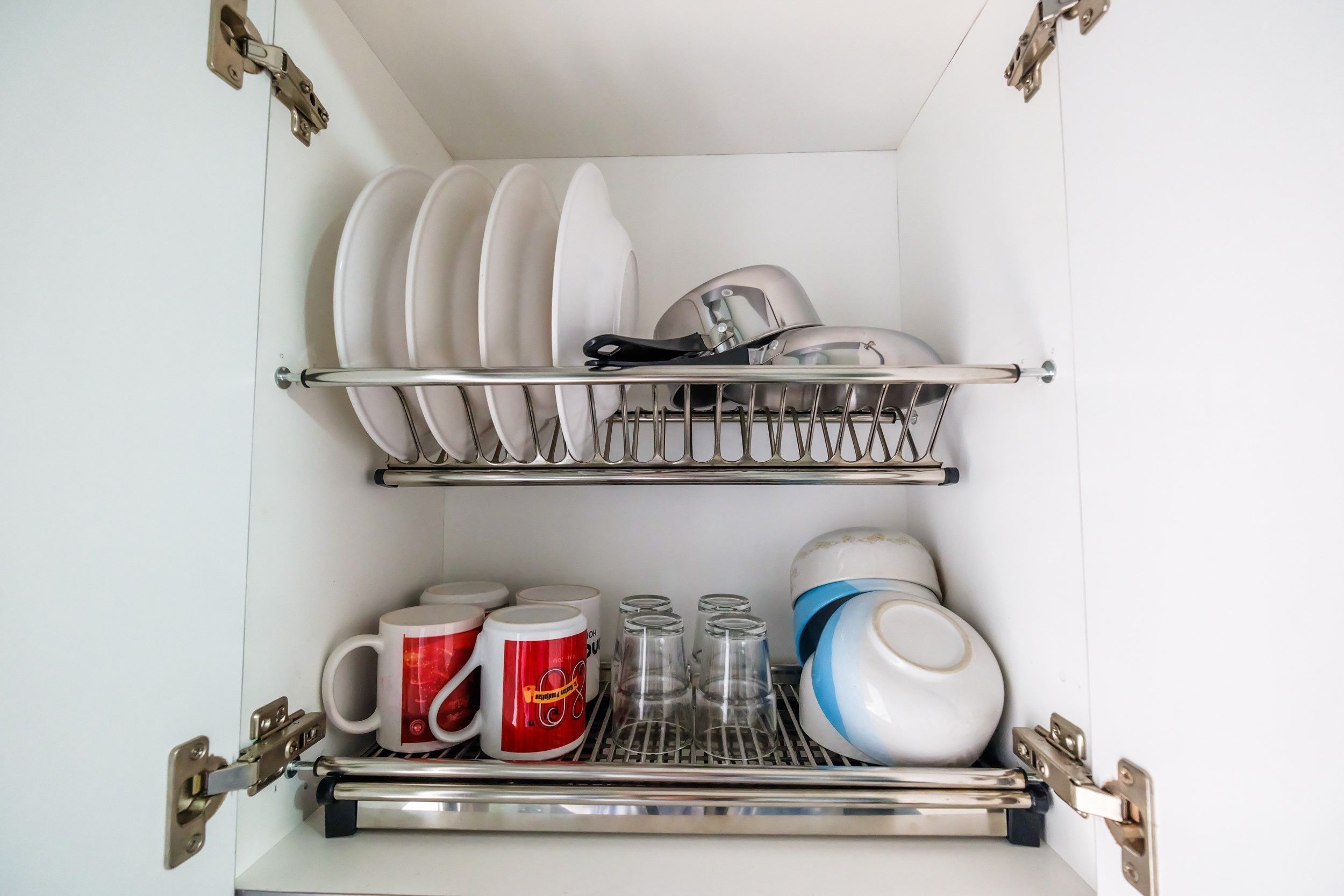 A kitchen with a dish rack holding plates and a shelf with mugs and glasses.