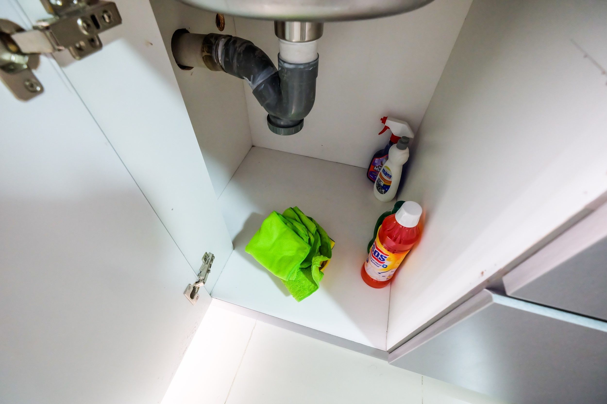 A bathroom sink with a pipe, a green cloth, and two bottles of cleaning products.
