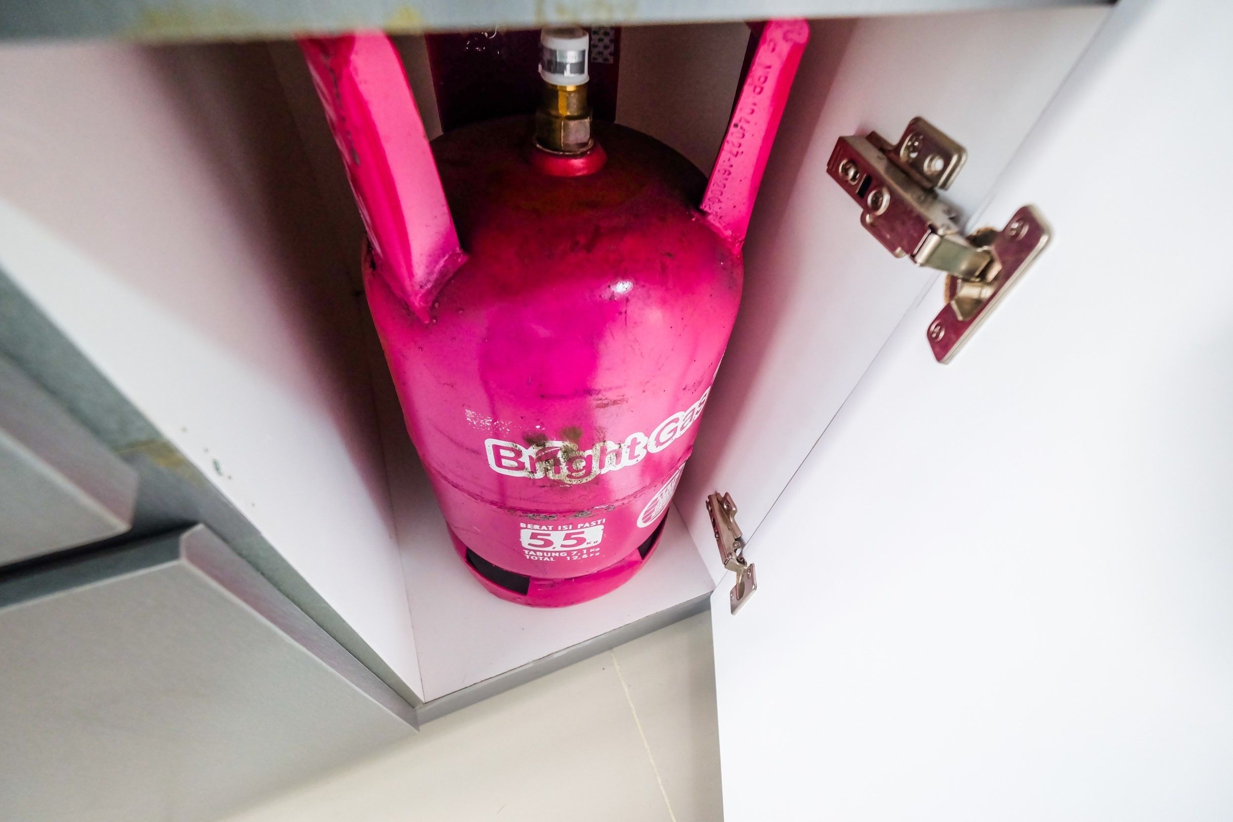 A pink gas cylinder labeled "BrightGas" under a cabinet.