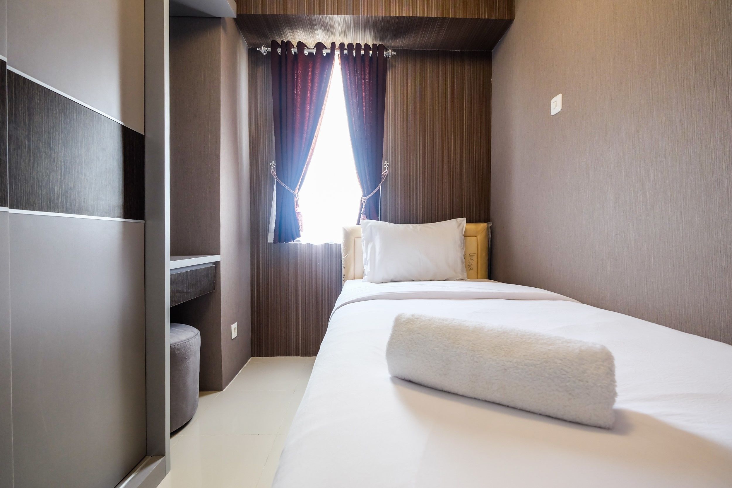 A hotel room with a neatly made bed, a small seating area, and a window with curtains.