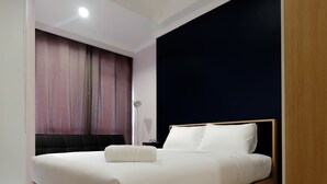 A modern hotel room with a wooden bed frame, white bedding, and a dark accent wall. - Comfortable Studio at Menteng Park Apartment (Jakarta)