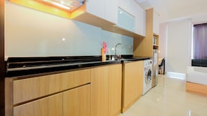 A modern kitchen with wooden cabinets, a black countertop, and a built-in washing machine. - Comfortable Studio at Menteng Park Apartment (Jakarta)