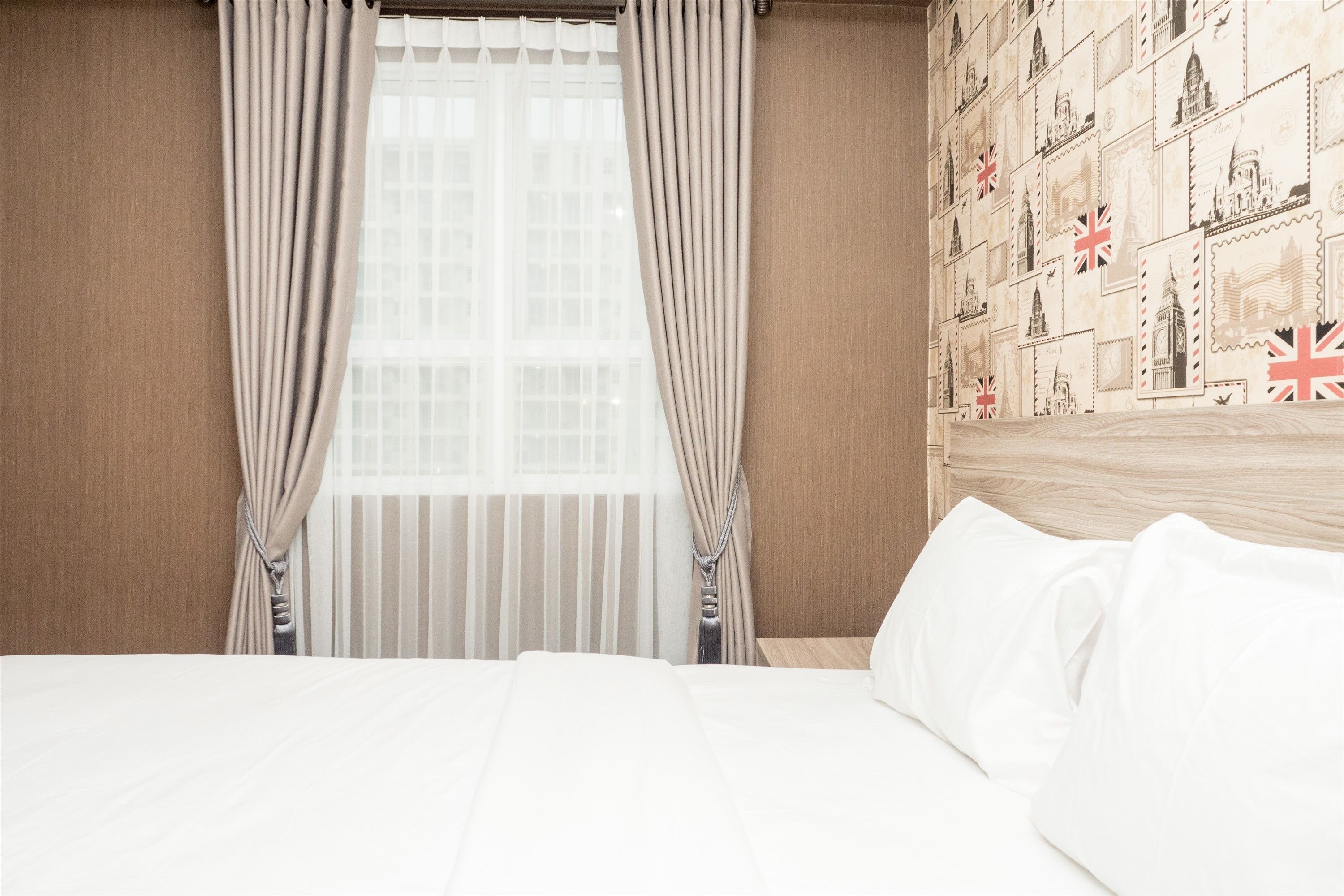 Habitación de hotel con una cama grande, cortinas, una ventana con persianas y una pared decorada con sellos postales.