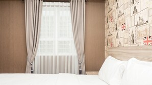 Ett hotellrum med en stor säng, gardiner, ett fönster med persienner och en vägg som är dekorerad med frimärken.