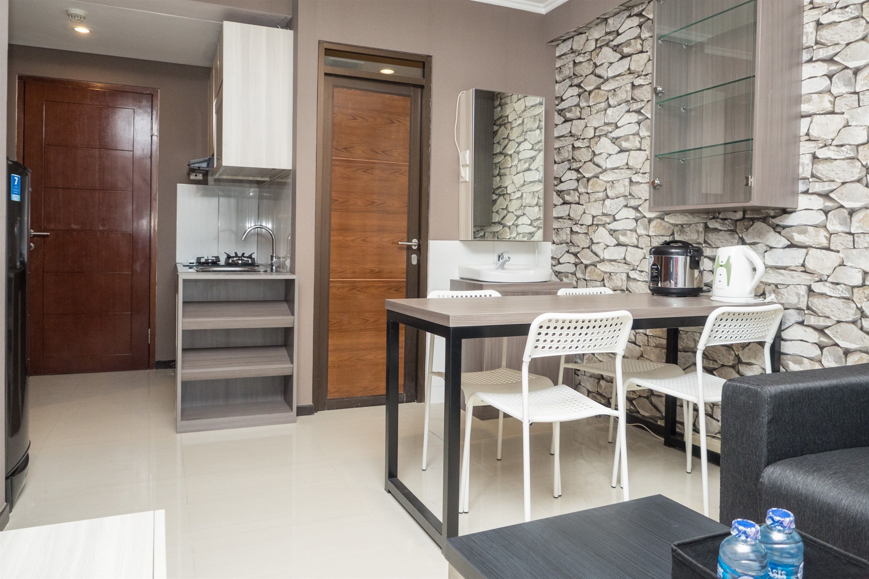 Una cocina compacta con salpicadero de pared de piedra, una zona de comedor con mesa y sillas, y un sofá negro en la sala de estar.