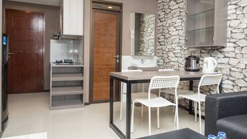 Una cocina compacta con salpicadero de pared de piedra, una zona de comedor con mesa y sillas, y un sofá negro en la sala de estar.