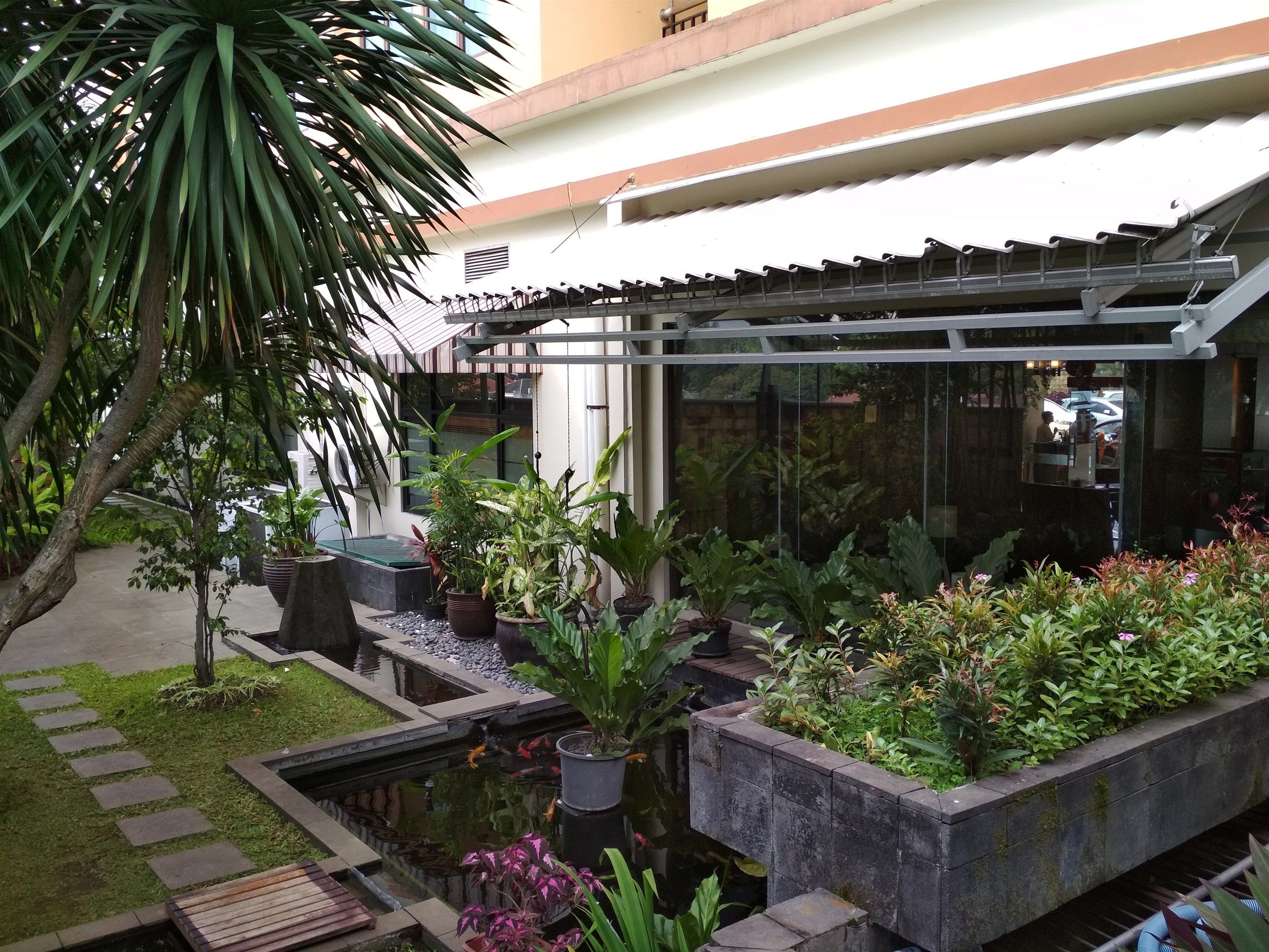 A courtyard with a koi pond, potted plants, and a pergola structure.