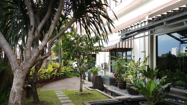 A modern building with a glass facade, a garden with a koi pond, and a pathway.
