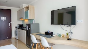 Une cuisine compacte équipée d’un réfrigérateur, d’un four à micro-ondes et d’un lave-linge. On y trouve une table à manger avec deux chaises, ainsi qu’un téléviseur à écran plat fixé au mur.