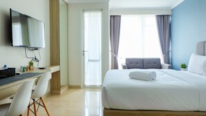Une chambre d’hôtel comprenant un lit, un bureau avec des chaises, une télévision et une fenêtre avec des rideaux.