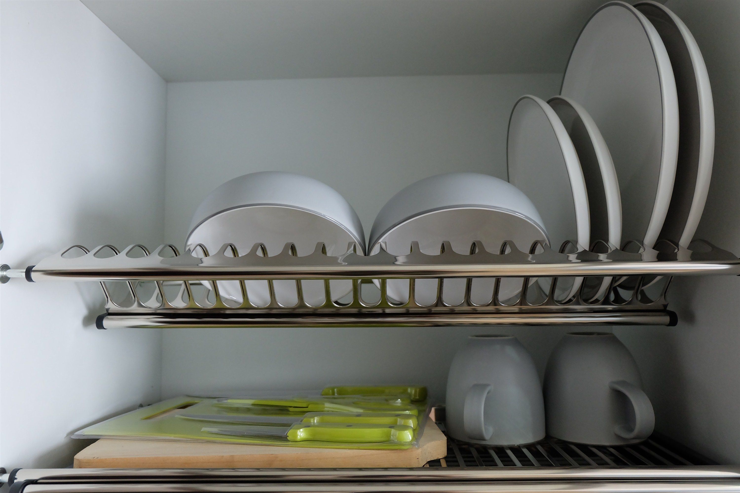 A kitchen with a dish rack holding plates and bowls, a kettle, and a cutting board with knives.