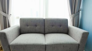 Un canapé gris, recouvert d’un tissu texturé, placé devant une fenêtre ornée de rideaux légers.