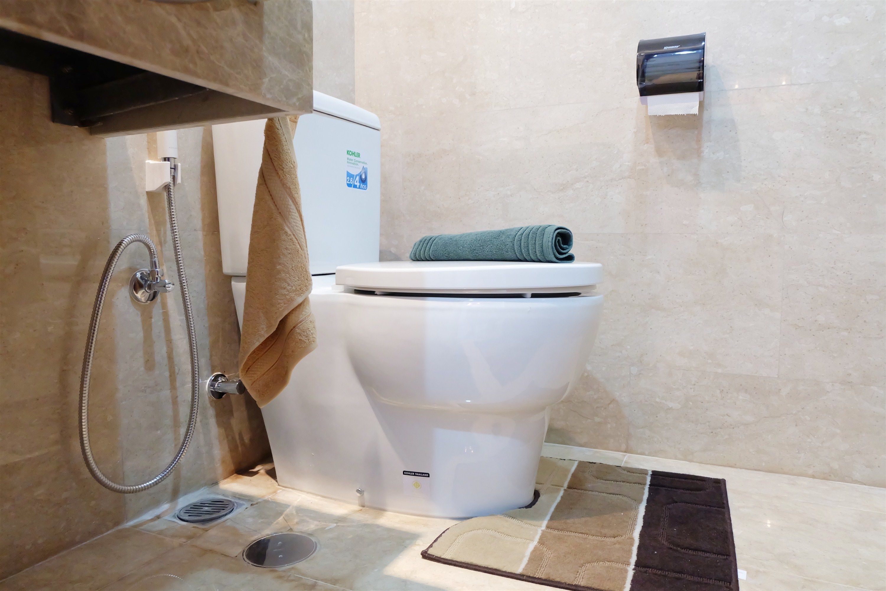 A bathroom with a toilet, a towel, a hand dryer, and a showerhead.