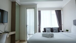 A hotel room with a bed, a desk, a TV, and a view of the city through the window. - Comfy Studio Menteng Park Apartment (Jakarta)