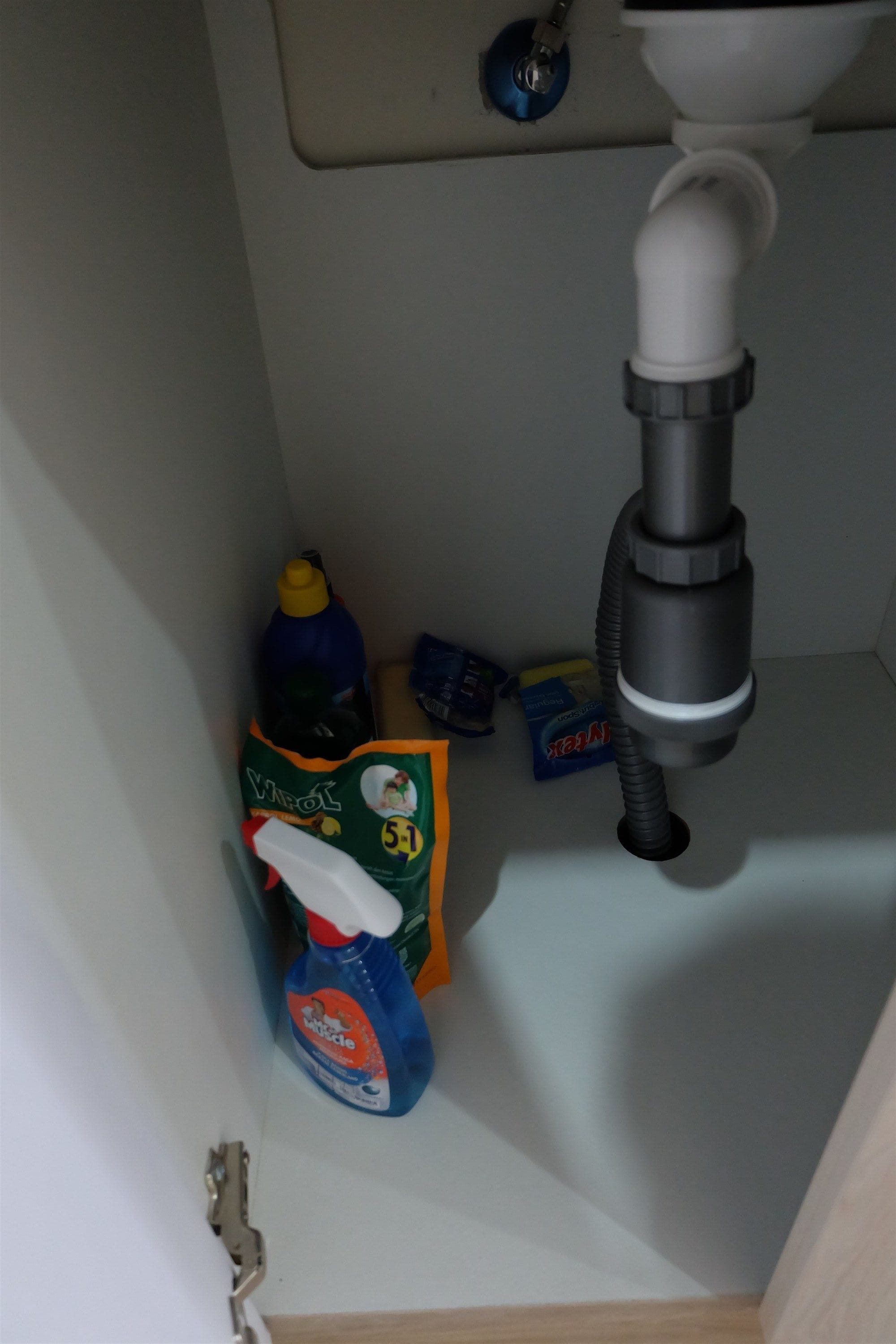 Un lavamanos con desagüe, una botella de detergente, una botella de jabón para manos y una caja de papel higiénico.