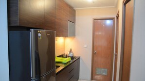 A compact kitchen with dark wooden cabinets, a stainless steel refrigerator, and a small countertop with a kettle and dish rack. - Great Location 2BR Maple Park Apartment (Jakarta)
