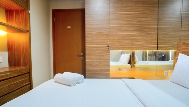 A hotel room with a wooden wardrobe, a bed with white linens, and a mirror reflecting the room. - Great Location 2BR Maple Park Apartment (Jakarta)