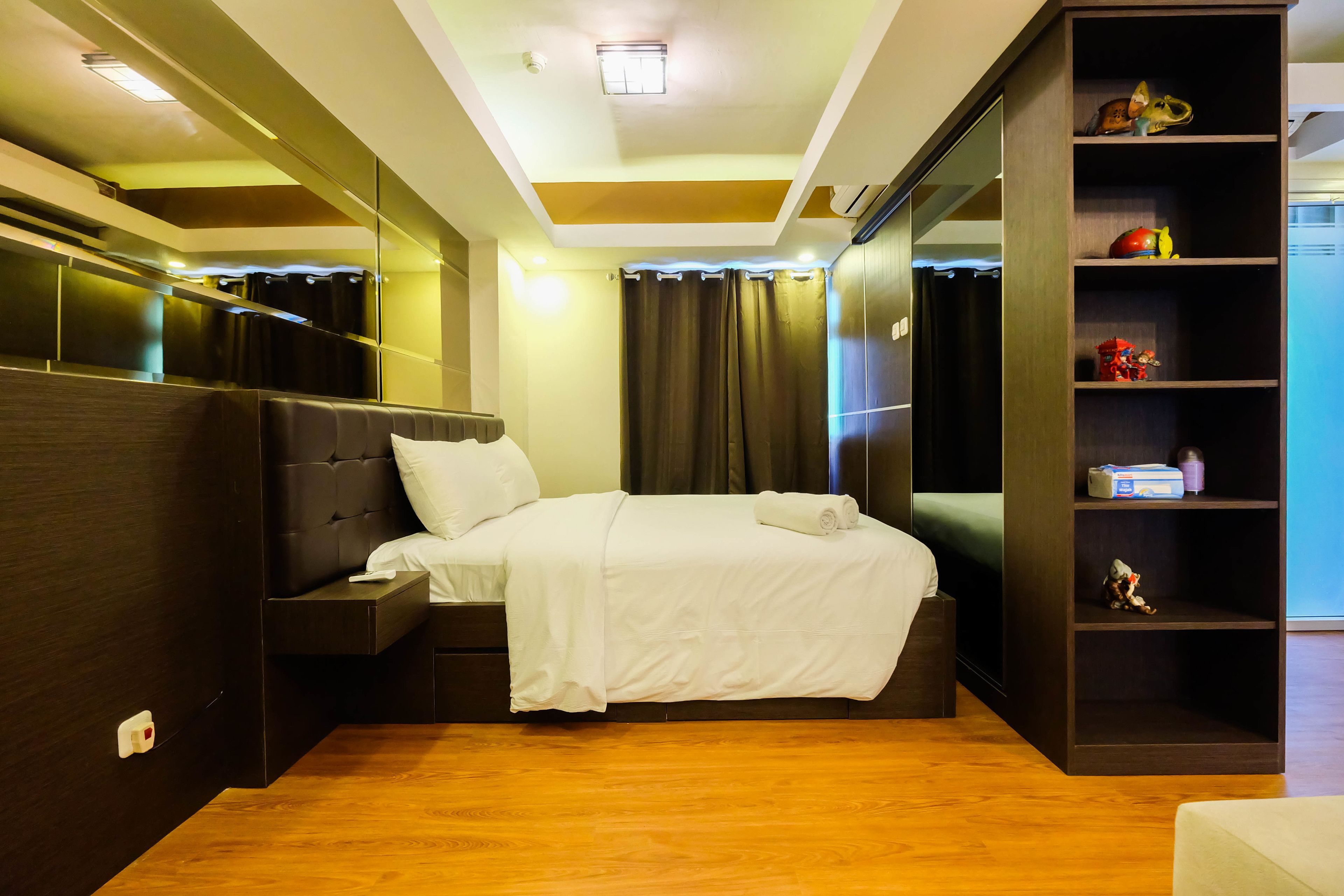 Een moderne hotelkamer met een net opgemaakt bed, een inbouwkast en een klein plankje met persoonlijke spullen.