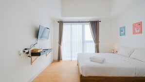 Une chambre à coucher avec un lit, un téléviseur fixé au mur, un bureau avec un ordinateur et une fenêtre avec des rideaux.