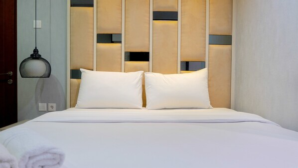 A neatly made bed with two pillows, a wall-mounted light fixture, and a door with a handle.
