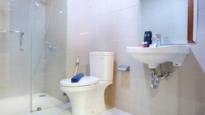 A bathroom with a glass-enclosed shower, a toilet, and a sink with toiletries. - Exclusive 2BR Springhill Terrace Residences (Jakarta)