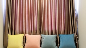A sofa with four cushions in yellow, pink, blue, and teal colors, positioned in front of a curtain with a metallic sheen. - Artistic Studio Apartment at The Oasis Cikarang (Cikarang)