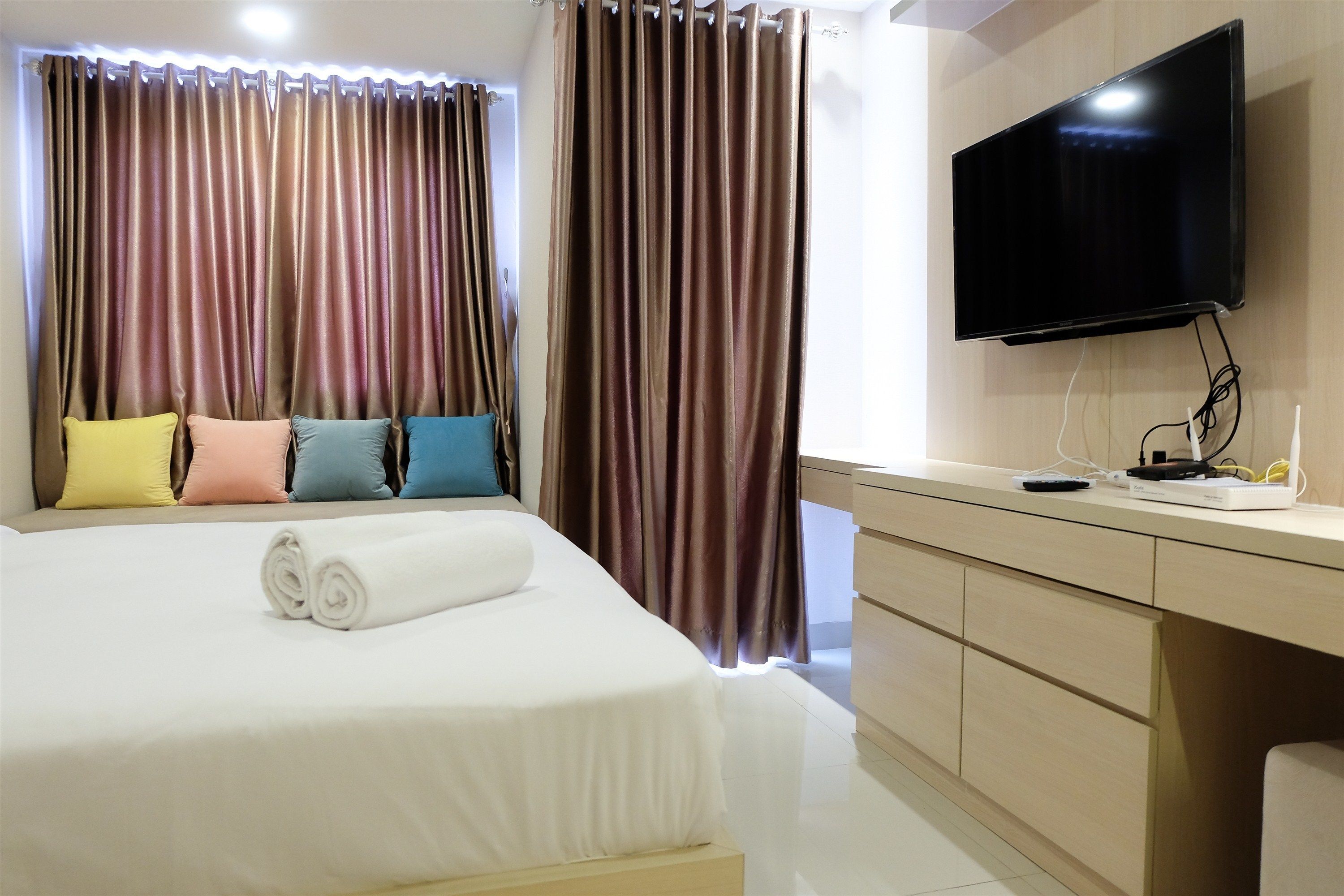 Een hotelkamer met een bed, een aan de muur bevestigde televisie en een bureau met een computer en andere spullen.