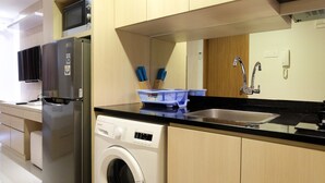 A modern kitchen with a stainless steel refrigerator, a built-in washing machine, a microwave, and a sink with a faucet. - Artistic Studio Apartment at The Oasis Cikarang (Cikarang)