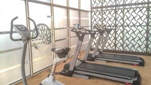 A gym with treadmills and a stationary bike, large windows, and a patterned wall. - Artistic Studio Apartment at The Oasis Cikarang (Cikarang)