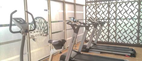 A gym with treadmills and a stationary bike, large windows, and a patterned wall.