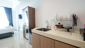 A modern kitchen with a sink, a dish rack, and a stove. There is a bed with a blue curtain in the background. - Fabulous Tree Park City Studio Apartment near ICE BSD (Tangerang)