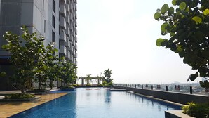 A swimming pool with a tiled edge, surrounded by a low wall and greenery. - Fabulous Tree Park City Studio Apartment near ICE BSD (Tangerang)