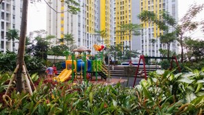 A playground with slides and climbing structures, surrounded by greenery and tall residential buildings in the background. - Furnished Studio Apartment @ The Springlake Summarecon (Bekasi)