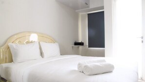 A neatly made bed with white linens and rolled towels, a bedside table with a black object, and a window with a view of the outside. - Furnished Studio Apartment @ The Springlake Summarecon (Bekasi)